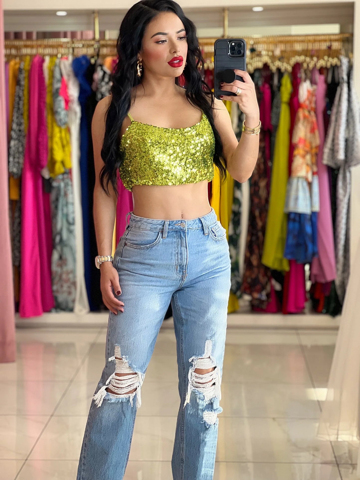 Woman in a lime green sequin crop top and light wash ripped jeans.
